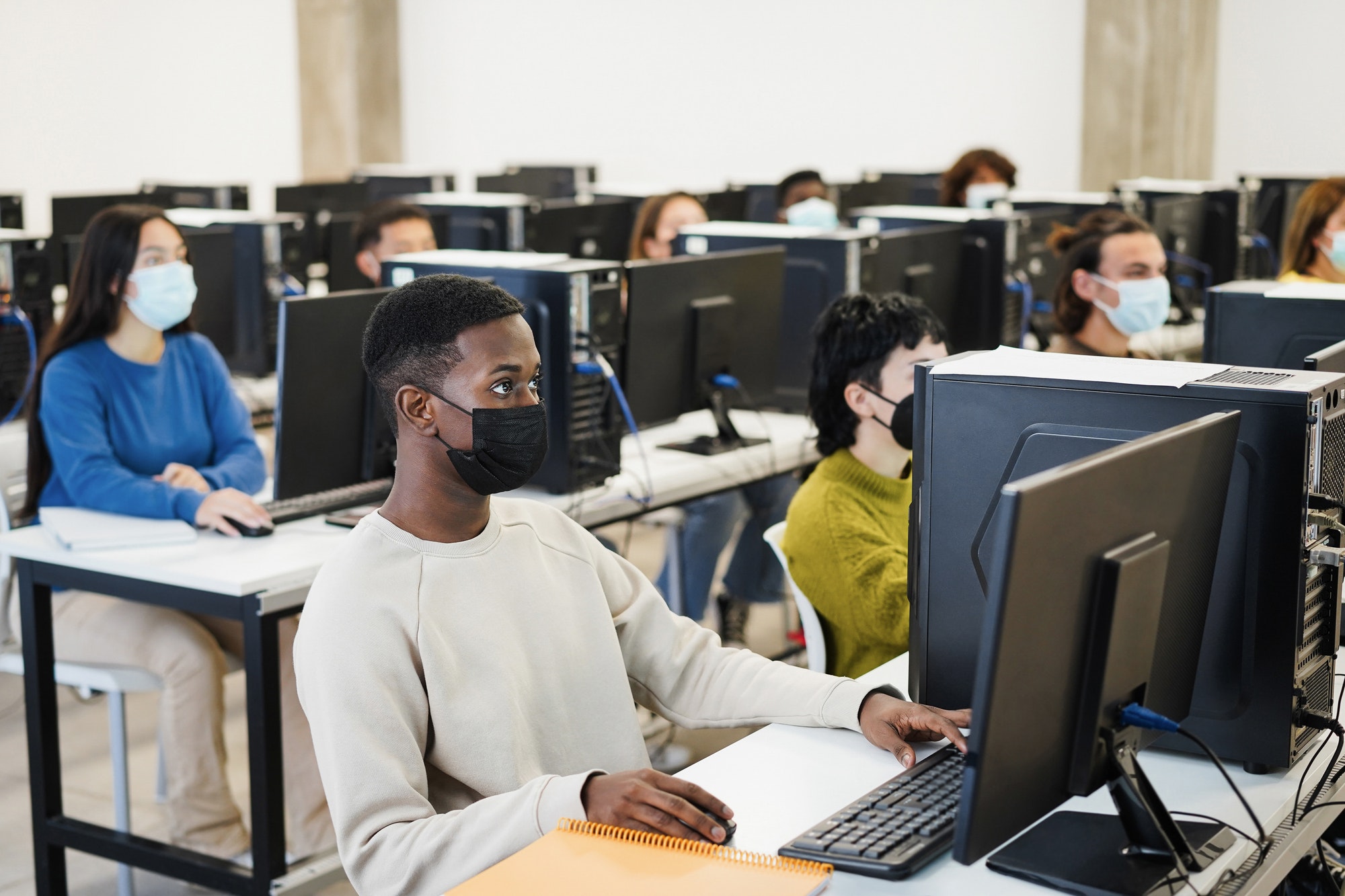 Multiracial young students using computers inside class room wearing safety masks